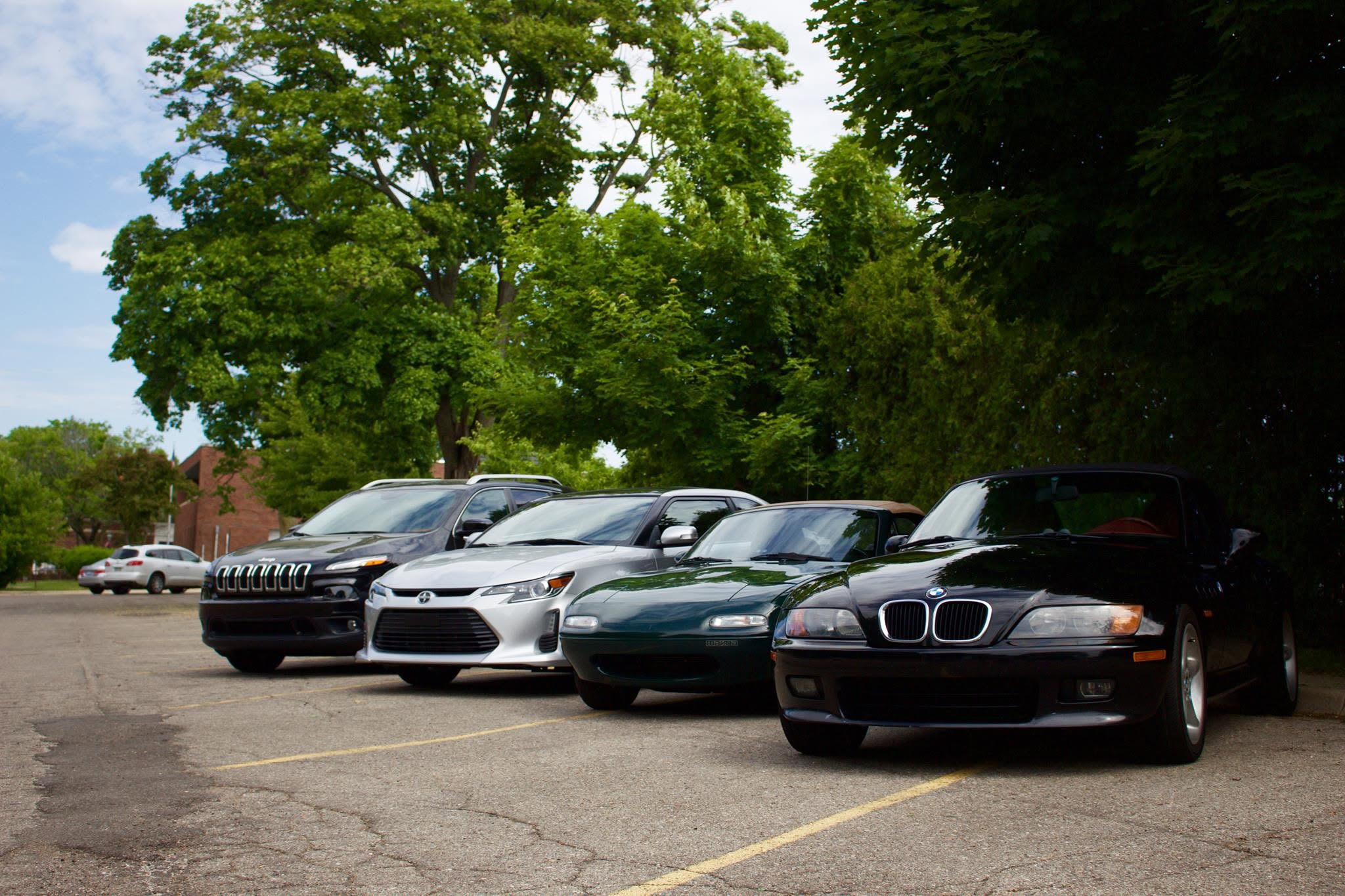 Four cars lined up in a parking lot at the first Baseline Rally — a black Jeep Cherokee, a silver Scion tC, a dark green Mazda Miata, and a black BMW Z3 roadster.
